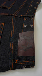 Close-up of dark denim jeans with a brand label on a light gray background