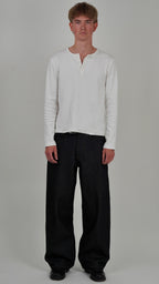 Person wearing a light gray long-sleeve shirt and black pants on a plain background