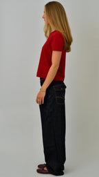 Woman wearing a red shirt and black pants standing against a white background