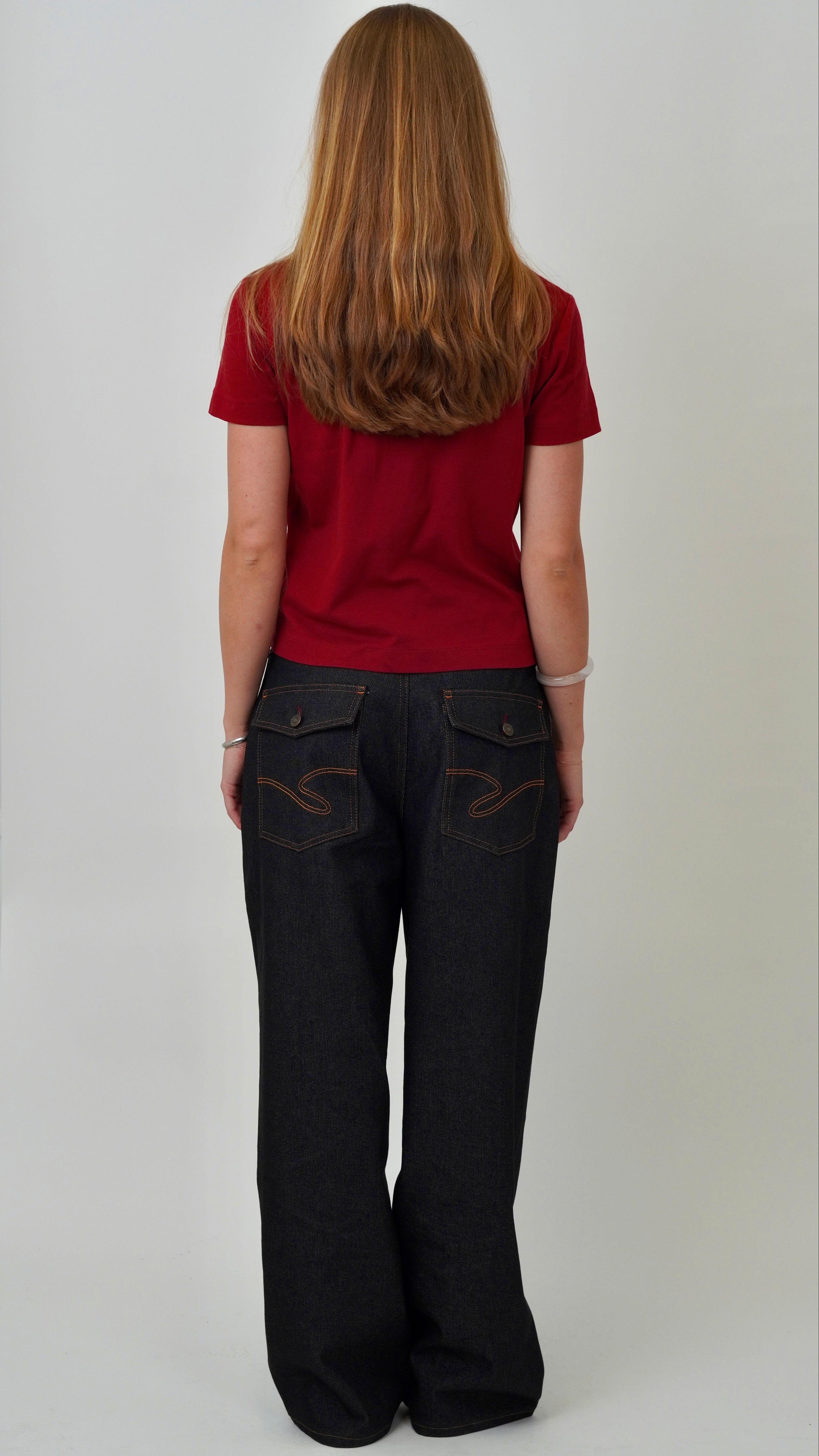 Person wearing a red shirt and black pants with decorative stitching on a plain background