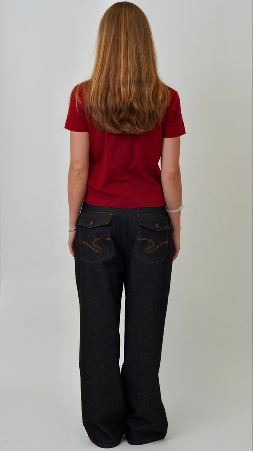 Person wearing a red shirt and black pants with decorative stitching on a plain background