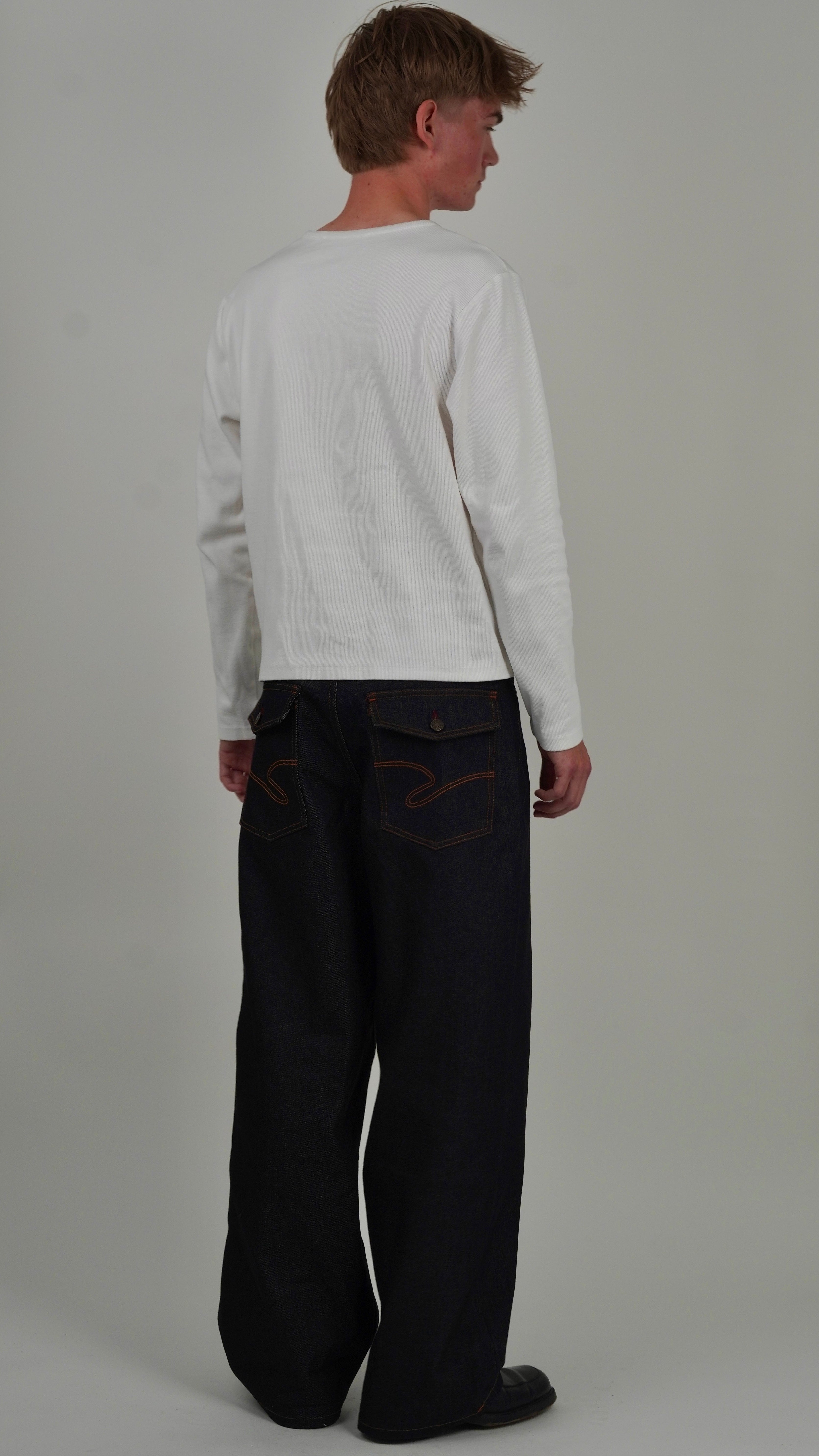 Person wearing a white long-sleeve shirt and dark pants on a plain background