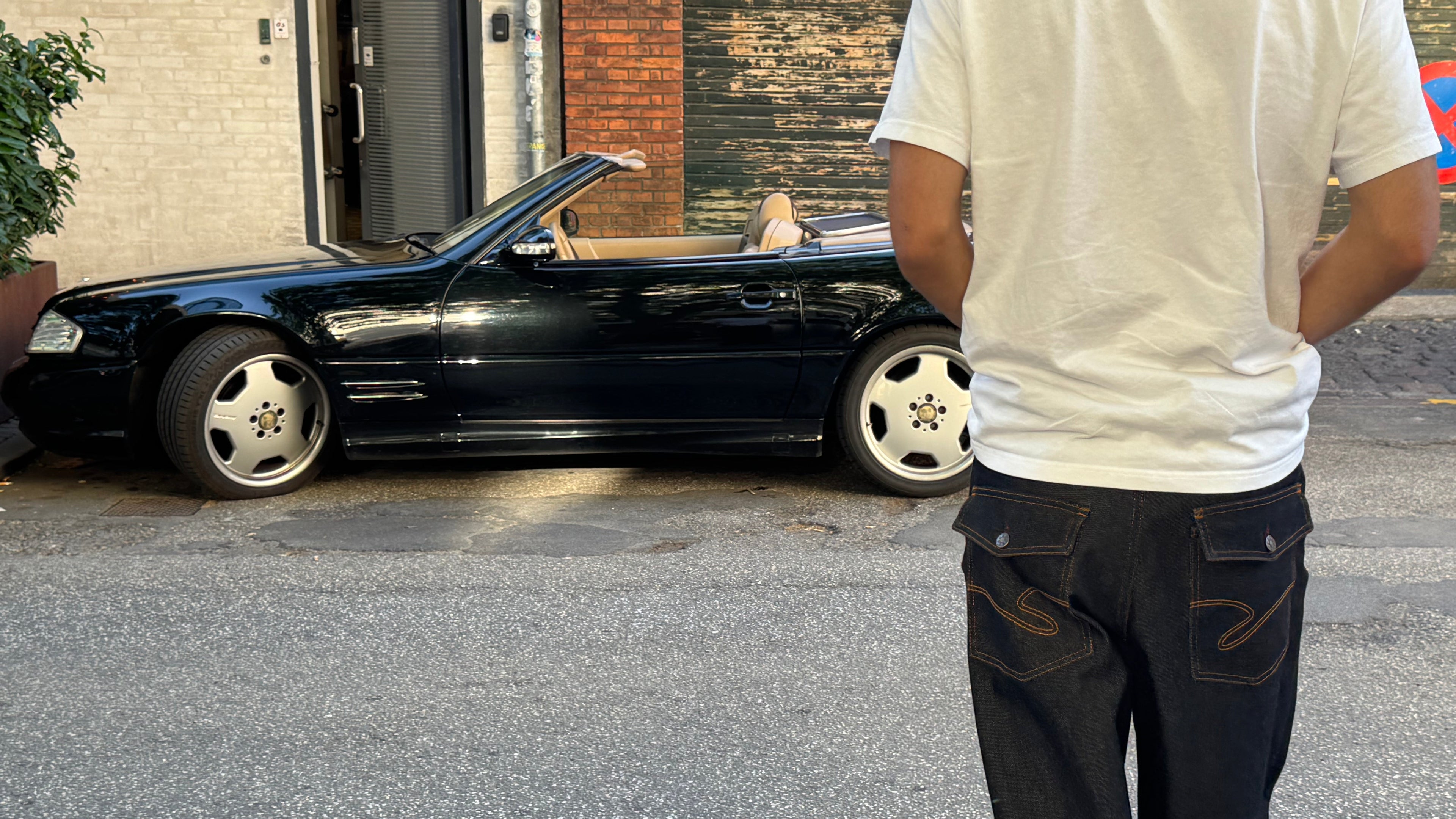 Person standing in front of a black convertible car on a street.
